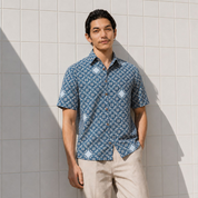 Man wearing blue printed batik shirt, posing by the wall outside with his hand in his pocket