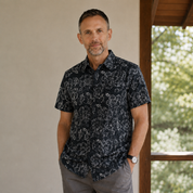 Man wearing black printed batik shirt with hibiscus print, posing indoors while indoors