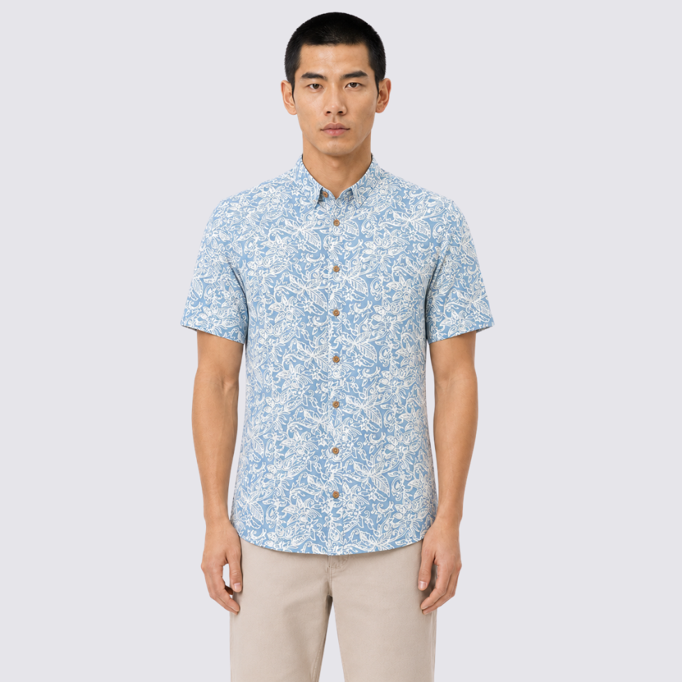 A man modeling a short-sleeve button-up shirt with a light blue and white floral pattern, paired with beige pants, against a solid light gray background.