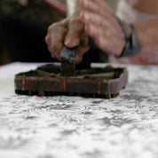 Person using a traditional wooden stamp on a textured surface