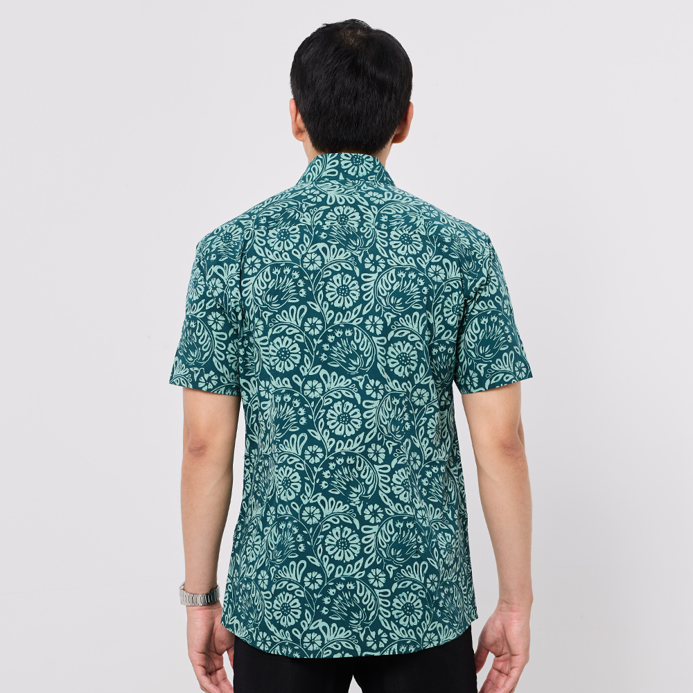 Person wearing a green patterned Batik shirt on a plain background