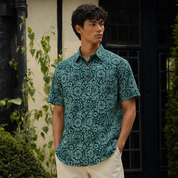 Man wearing teal printed batik shirt, posing outdoors with his hands in his pockets