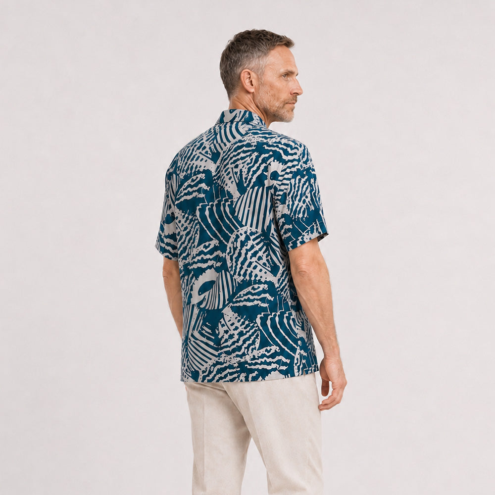 A man wearing a blue button-up shirt with a blue shell pattern, facing his back on a white background.

