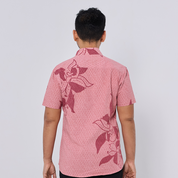 Person wearing a pink patterned shirt with floral designs on a plain background