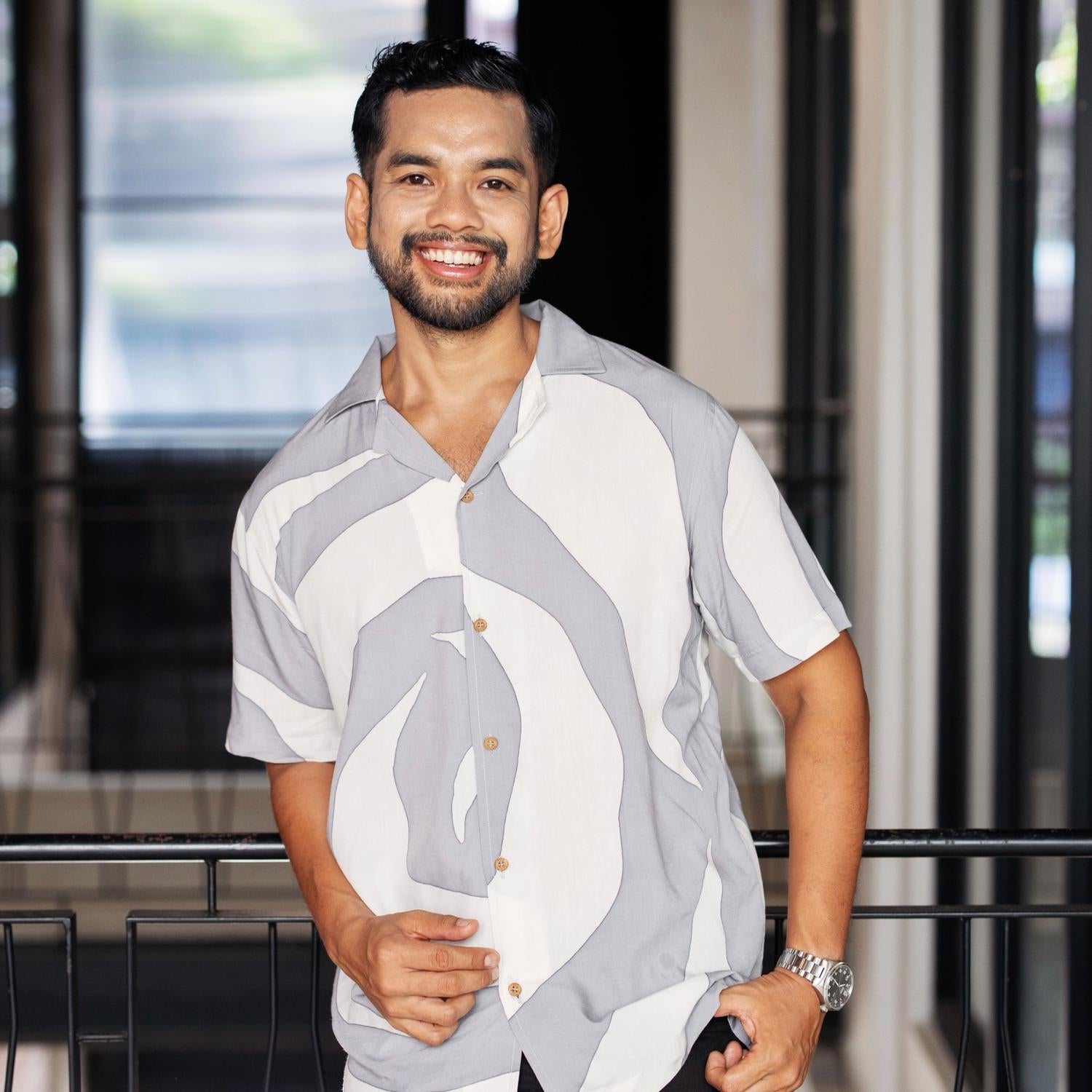 Man wearing a patterned shirt standing indoors with blurred background