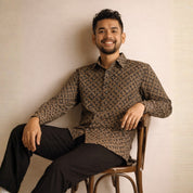 Man sitting on a chair wearing a patterned batik shirt against a beige wall