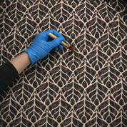 Person wearing a blue glove applying a brown substance to a textured surface with a tool.
