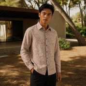 Man wearing a patterned shirt standing outdoors with trees and a building in the background
