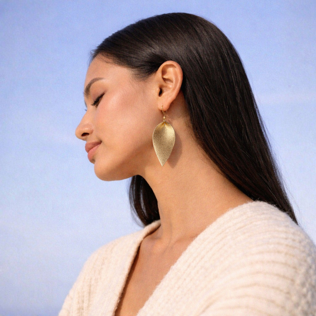 Woman wearing gold leaf-shaped earrings against a blue sky background