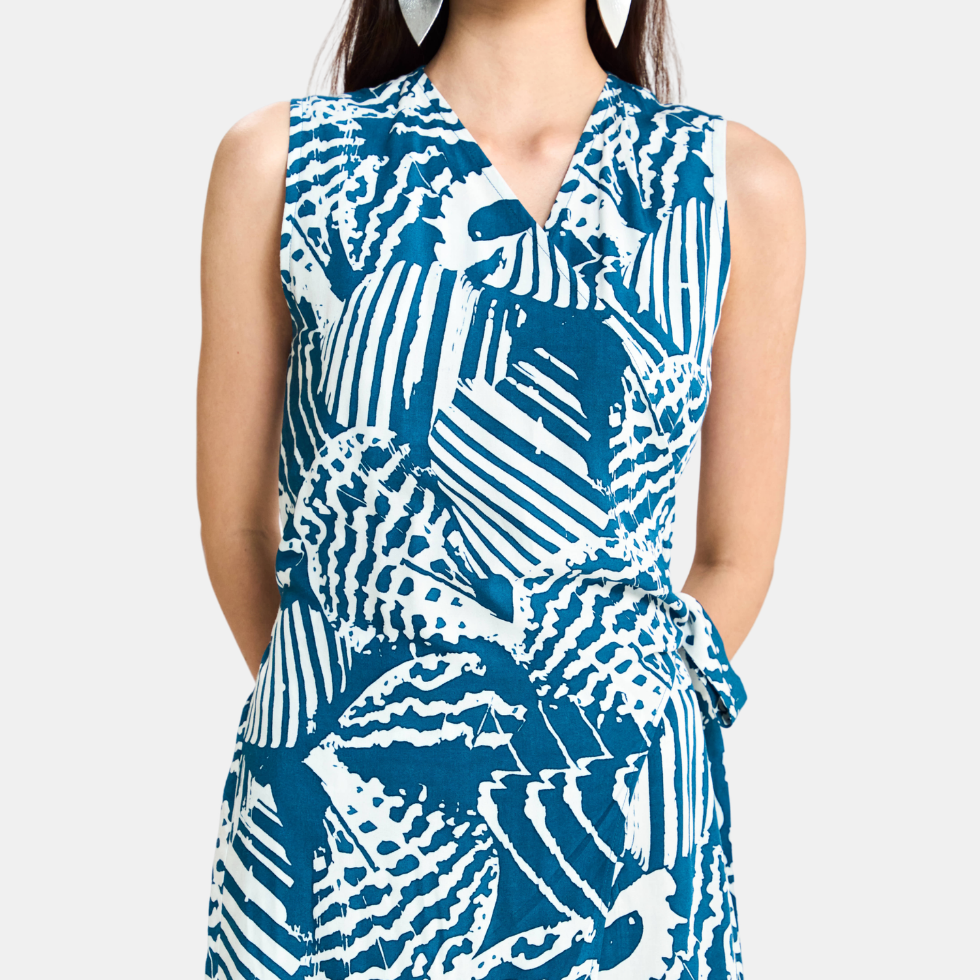 A sleeveless wrap-style dress with a bold blue and white abstract pattern, featuring a V-neckline and side tie detail, shown on a model against a light gray background.