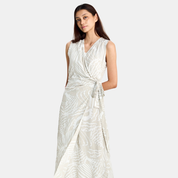 A woman modeling a sleeveless wrap-style maxi dress with a tie waist and an abstract light gray and off-white pattern, set against a plain light gray studio background.