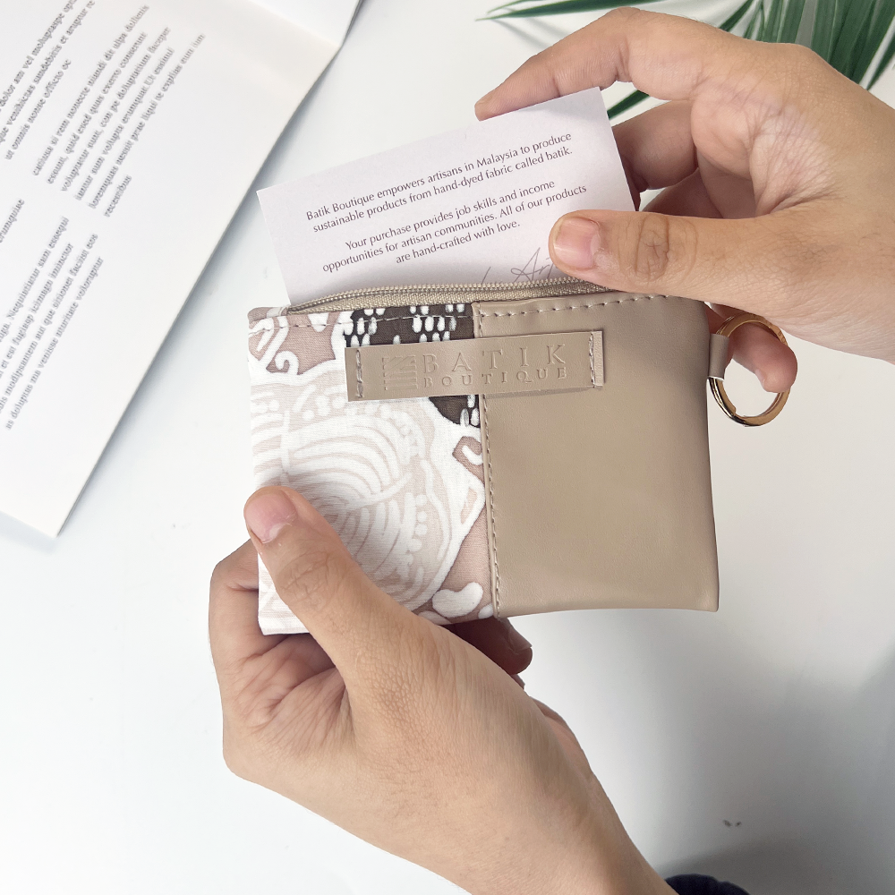 Person holding a beige wallet with a patterned interior, showing a close-up of the brand name.