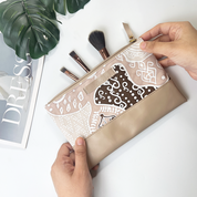 Beige makeup pouch with lace design being held open by hands on a white surface.