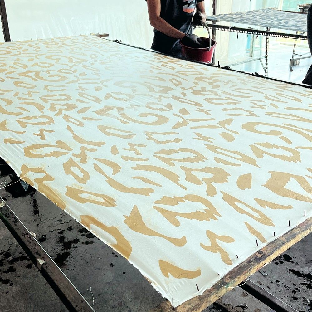 Sheet of paper with gold leaf design on a table, with a person in the background.