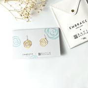 Gold earrings on a branded card with 'Embrace' and 'Batik Boutique' logos, placed on a white surface.