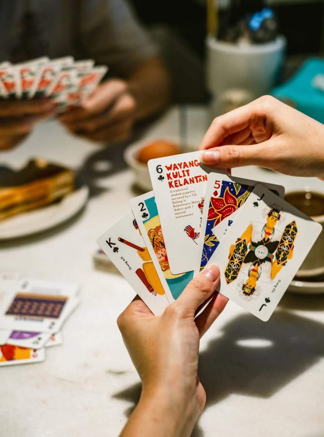Person holding playing cards with colorful designs on a table.