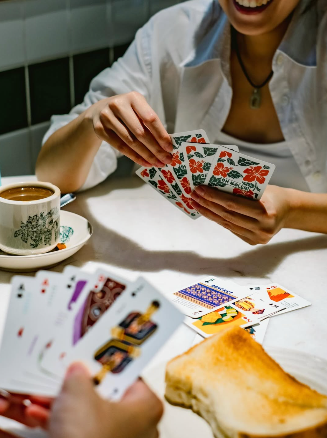 Person playing cards with a cup of coffee and toast on a table.