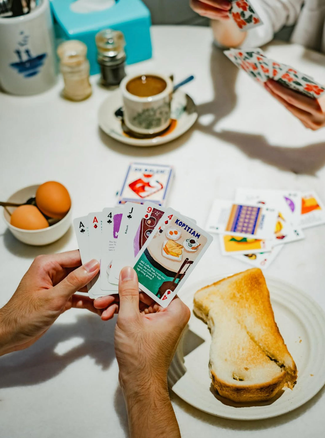 Two people playing cards at a table with toast, eggs, and coffee.