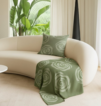 Green patterned throw blanket and pillow on a beige sofa in a living room with plants.