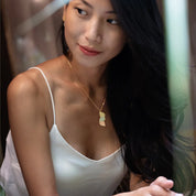 Woman wearing a white top and gold necklace with a pendant.