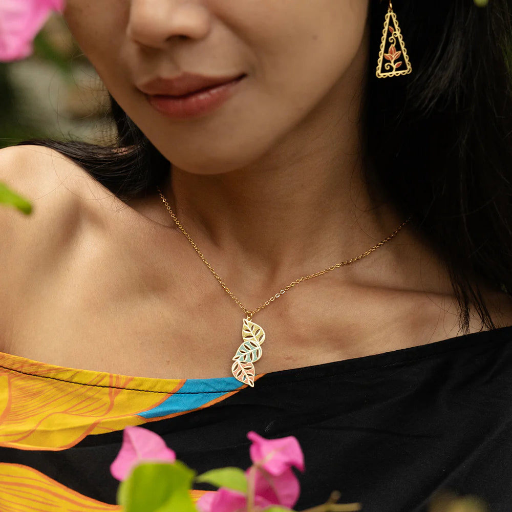 Woman wearing a gold necklace and earrings with flowers in the background