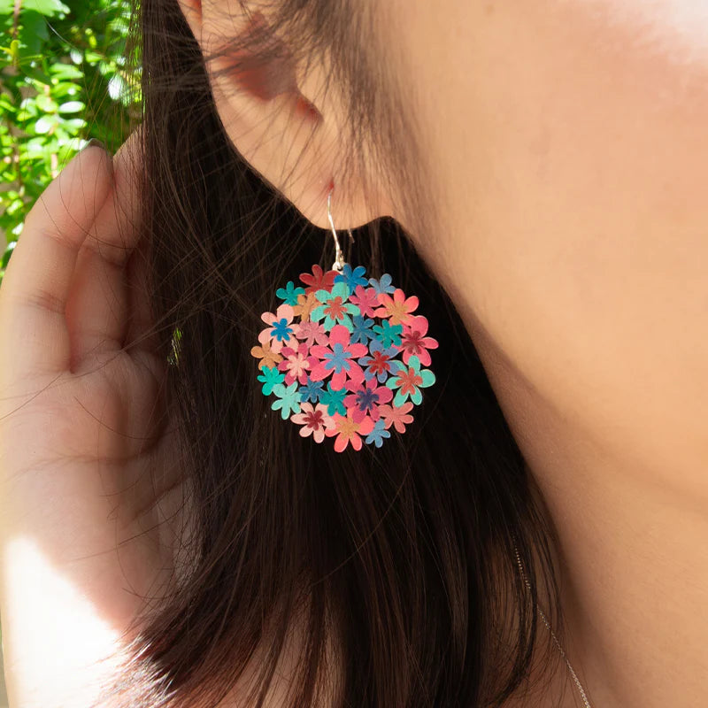 Colorful floral earrings worn by a person with a blurred natural background