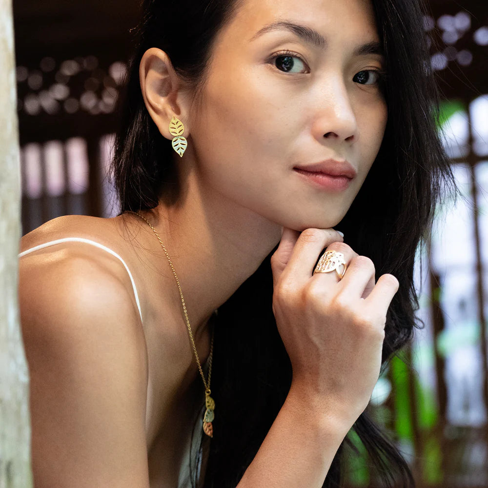Woman wearing gold earrings and a ring, with a blurred background