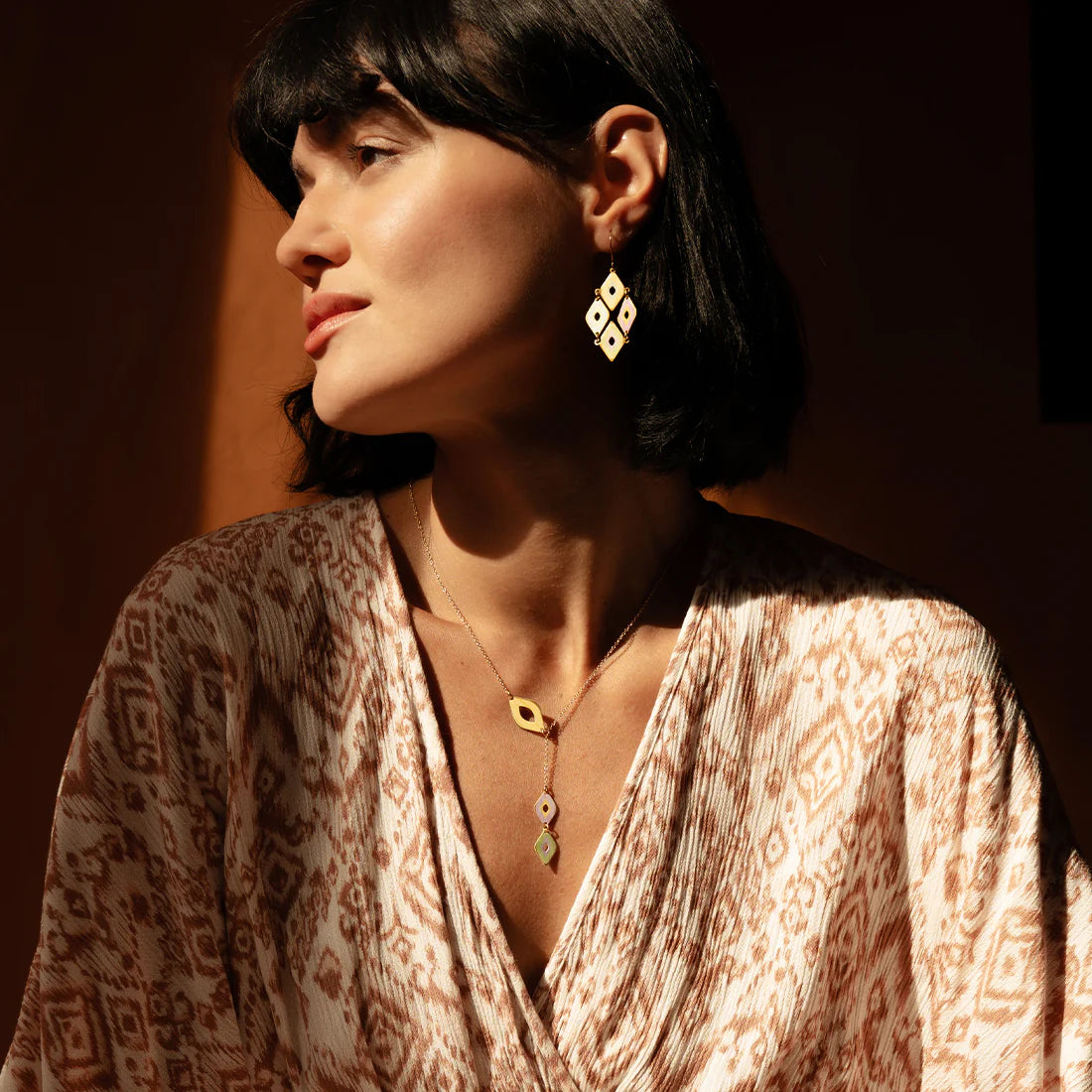 Woman wearing a patterned top and earrings with a warm light background