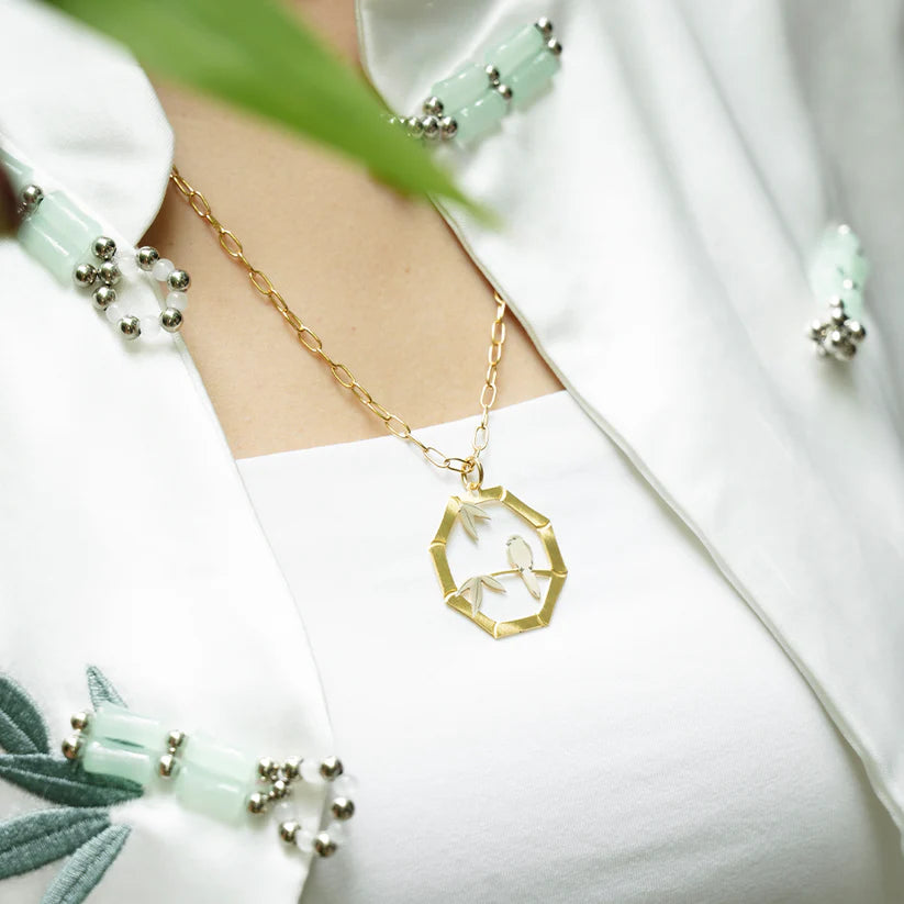 Gold necklace with a geometric pendant worn by a person in a white outfit.