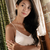 Woman wearing a white top with decorative earrings and necklace, standing in a room with curtains.