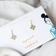 Jewelry packaging with floral earrings and brand logos on a soft fabric background