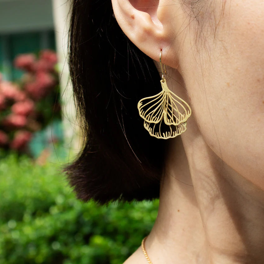 Gold ginko earring worn by a person with a blurred outdoor background