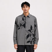Man wearing a gray shirt with black floral patterns on a white background