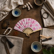 Pink tie-dye fan on a wooden surface with various items including bowls and fabric.