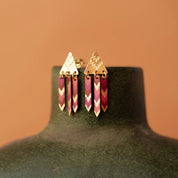 Gold and pink earrings on a green mannequin against a brown background