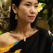 Woman wearing a colorful top with a floral headpiece, earrings, and necklace.