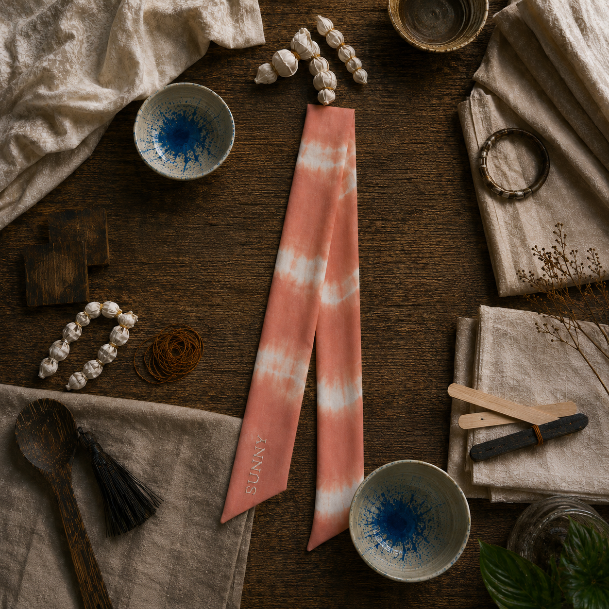 Tie-dye pink and white bandana on a wooden surface with various items.